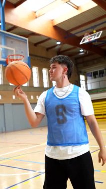 Genç basketbolcu parmak ucunda bir top çeviriyor. Yeteneğini ve kontrolünü bir spor salonunda sergiliyor.