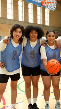 Çeşitli bayan basketbol oyuncuları kapalı sahada bir takım fotoğrafı için gülümsüyor ve poz veriyorlar.