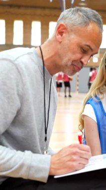 Basketbol koçu bir panoya bir oyun çiziyor ve oyun stratejisini iki bayan oyuncuya bir mola sırasında anlatıyor.