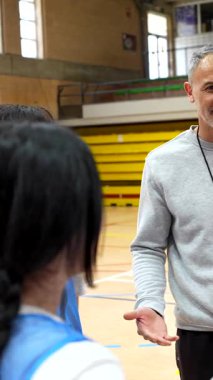 Tecrübeli basketbol koçu kadın takıma rehberlik ediyor, kapalı alan saha eğitimi sırasında oyun stratejisini tahtaya çiziyor.