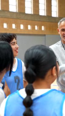 Basketbol koçu beyaz tahtayı kullanarak iç sahadaki bayan sporculara oyun stratejisini anlatıyor.