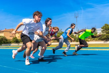 Parlak bir güneşin altında canlı mavi bir pistte koşan çeşitli atletler, yarışmada enerji ve kararlılık gösteriyorlar.