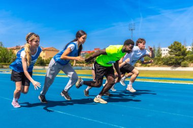 Genç sporcular parlak güneşin altında enerjik mavi bir pistte koşuyorlar. Kararlılıklarını ve rekabetçi ruhlarını sergiliyorlar.