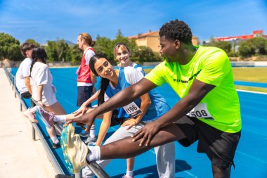 Koşucular bacaklarını güneşli bir pistte açıyorlar, yaklaşan yarışa hazırlanıyorlar ve rekabetin enerjisini kucaklıyorlar.