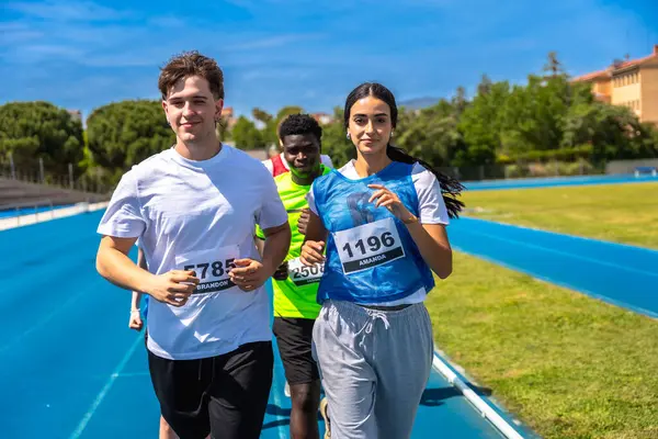 Bir spor müsabakası sırasında mavi pistte koşan bir grup sporcu, takım çalışmasını ve kararlılığını gösteriyor