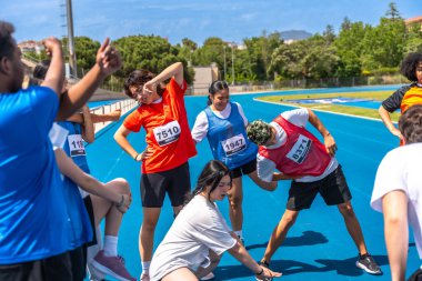 Önlük giyen gençler yarışmadan önce mavi bir pistte birbirlerine esniyorlar.
