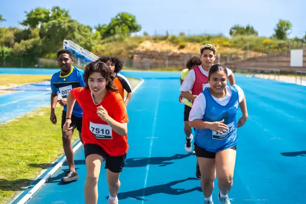 Mavi bir pistte koşan kararlı genç sporcular, bir pist ve saha yarışmasında zafer için çabalıyorlar.