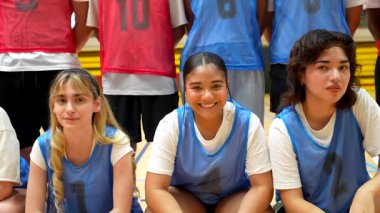 Çeşitli genç basketbol oyuncuları sahada bir takım fotoğrafı için gülümsüyor ve poz veriyorlar.