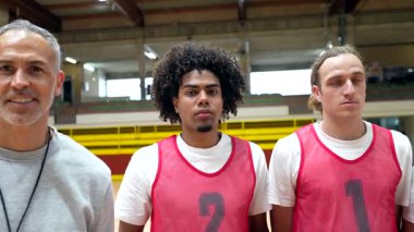 Çok ırklı basketbol takımı üyeleri ve antrenörleri bir jimnastik salonunda birlik ve çeşitlilik gösteriyorlar.