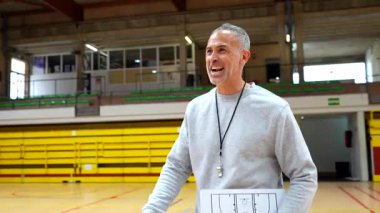 Basketbol koçu, oyun stratejisini beyaz tahta kullanarak ve sahada oyuncularıyla el sıkışarak açıklıyor.