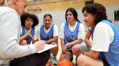 Yoğun mola sırasında takıma stratejik rehberlik sağlayan bayan basketbol koçu, oyun taktiklerini tartışıyor ve odaklanmış liderliğe sahip oyuncuları motive ediyor.