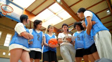 Stratejik takım molasında genç sporculara rehberlik eden profesyonel bayan basketbol koçu, spor salonu ortamında odaklanmış kararlılıkla taktiksel sezgileri paylaşıyor.