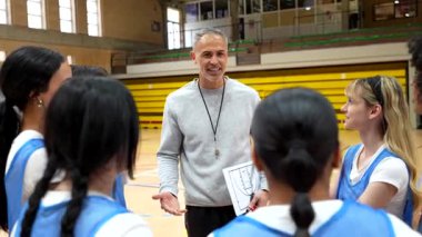Spor salonundaki kadın takıma beyaz tahta kullanarak oyun stratejisini açıklayan deneyimli basketbol koçu.