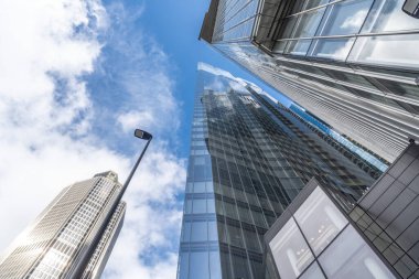 Londra 'nın finans bölgesindeki modern gökdelenlerin alçak açılı görüntüsü, bulutlu mavi gökyüzüne karşı yükselen varlıklarını sergiliyor.