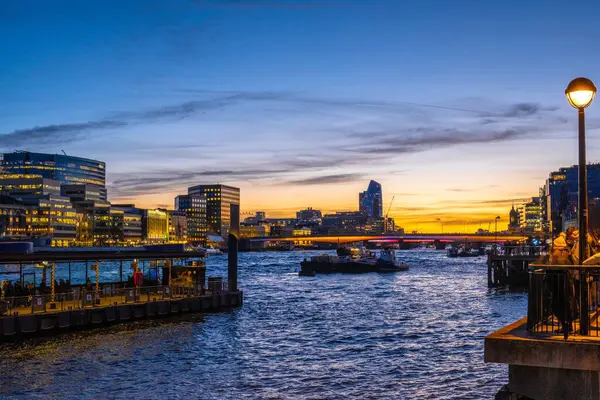Gün batımında Londra 'nın aydınlık ufuk çizgisi suları yansıtırken römorkörler Thames' de yelken açıyorlar.