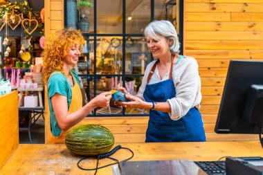 Çiçekçide karpuz, küçük işletme ve elektronik ödeme konsepti için temassız kredi kartıyla ödeme yapan mutlu bir müşteri.