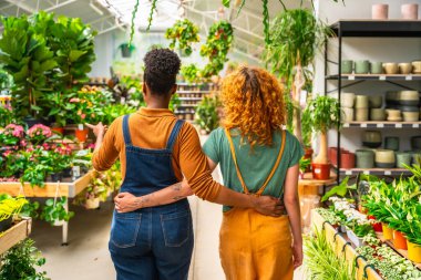 Bir bahçe merkezinde çalışan ve satılık bitkileri tartışan iki genç kadın, arkadan görüldü.