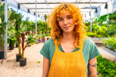 Çevresi gelişen bitkilerle çevrili canlı bir serada çalışan kendine güvenen genç kadın bahçıvan ve bahçecilik tutkusu.