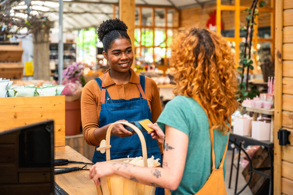 Friendly shop assistant holding credit card reader while customer making contactless payment in a flower shop