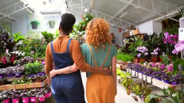 İki kadın çiçekçi çiçekçinin dükkanlarında yürüyorlar ve sarılıyorlar, gülümsüyorlar ve kameraya bakıyorlar.