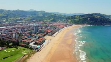 Zarautz, gipuzkoa 'nın hava perspektifi, altın plajı, turkuaz suları ve kıvrımlı yeşil tepelerin zeminine kurulmuş canlı şehir manzarasını sergiliyor.
