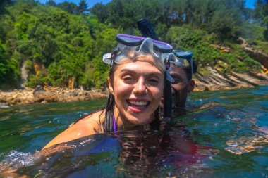 Okyanusta şnorkelle yüzen ırklar arası bir çift, canlı yeşil bir sahil şeridiyle çevrili, neşeli bir yaz macerasının tadını çıkarıyorlar.