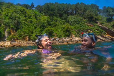 Şnorkelli maskeler takan turistler, güneşli bir yaz tatilinde berrak okyanus sularında eğlenirken neşeyle gülüyorlar.