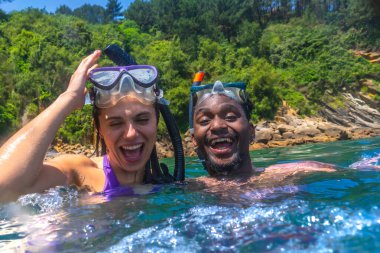 Irklar arası çift, canlı okyanusta şnorkelle yüzerek eğleniyor, yaz tatili boyunca gülüyor ve neşeli anları paylaşıyor.