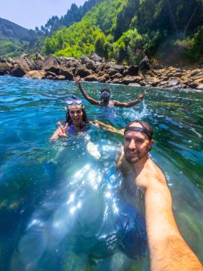 Üç arkadaş ferahlatıcı okyanus suyunda şnorkelle yüzmeyi, güzel bir kıyı manzarasının ortasında selfie çekmeyi severler.
