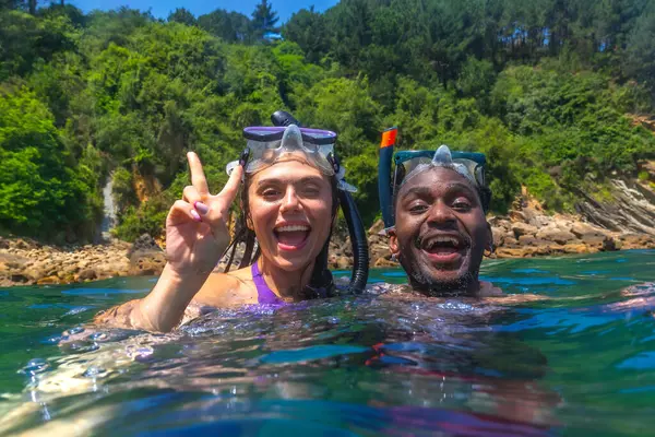 Genç çok ırklı çift kristal berrak tropikal denizde birlikte şnorkelle yüzmekten zevk alıyor. Kadın zafer işareti yapıyor.