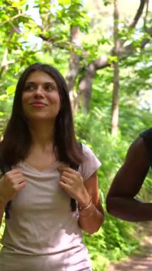 Bereketli ormanda yürüyüş yapan, güneşli patikada yürürken neşeli anları paylaşan, sırt çantaları ve güneş gözlükleri takan, birlikte doğanın tadını çıkaran çok ırklı bir çift.