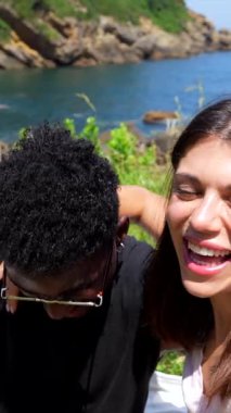 Genç, çok ırklı bir çift deniz kenarında romantik bir piknik yaparken kiraz yiyip selfie çekiyor.