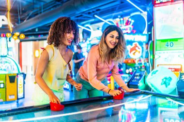 İki genç kadın renkli neon ışıklarla aydınlatılmış canlı bir oyun salonunda hokey oynuyorlar.