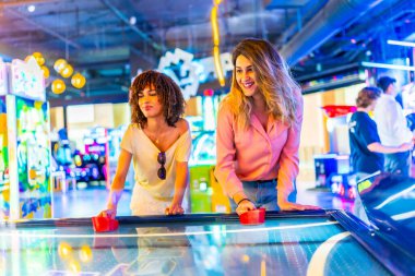 Canlı bir oyun salonunda hava hokeyi oynarken konsantre olan iki bayan arkadaş, boş zamanlarının tadını çıkarıyorlar.