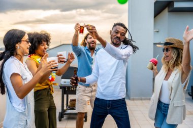 Neşeli arkadaşlar coşkulu bir çatı partisinde kadeh kaldırıyor ve dans ediyorlar. Güneş şehrin üzerinde batarken içkilerin ve kahkahaların tadını çıkarıyorlar.