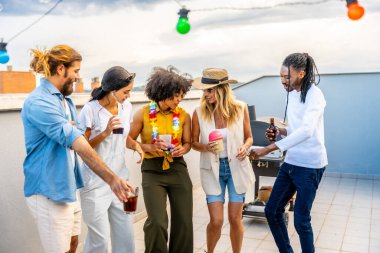 Neşeli bir grup arkadaş içki içiyor, dans ediyor ve çatıdaki barbekü partisinde sosyalleşiyorlar.