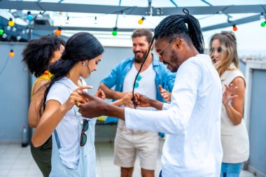 Gençler canlı bir çatı partisinde neşeyle dans ediyor, yaz atmosferinde ıslanıyor ve akşam ışıklarının altında birlikte kutlama yapıyorlar.