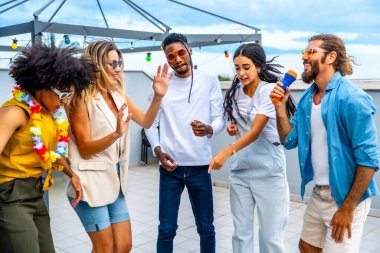 Bir grup neşeli çoklu etnik arkadaş çatıdaki bir partide karaoke söyleyip dans ederken eğleniyorlar.