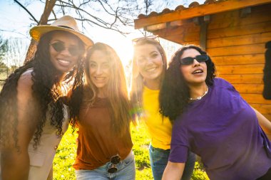 Dört farklı genç kadın gülümsüyor ve dışarıda kucaklaşıyorlar, gün batımının sıcacık ışığının tadını çıkarıyorlar ve arkadaşlıklarını kutluyorlar.