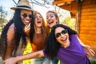 Dört çok ırklı bayan arkadaş parkta birlikte eğleniyor, gülüyor ve birbirlerinin arkadaşlığından keyif alıyorlar.