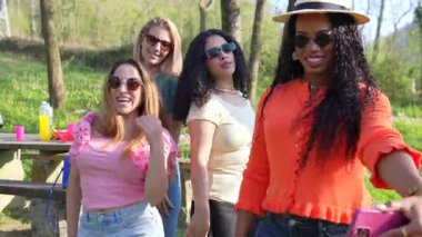 Çeşitli bayan arkadaşlar dans ediyor, selfie çekiyor, güneşli yaz günlerinde doğal park ortamında piknik yapıyorlar.