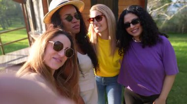 Kadın arkadaşlar birlikte neşeli anlar yakalıyorlar, güneşli bahçede gizli selfie çekiyorlar, gerçek dostluk ve çeşitli bağlar sergiliyorlar.