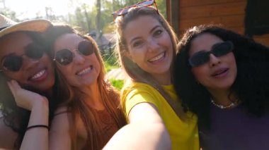 Neşeli çoklu etnik kadın arkadaşlar yaz anlarını yakalıyorlar, güneşli park ortamında neşeli selfie anıları yaratıp gerçek bağlantıları paylaşıyorlar.
