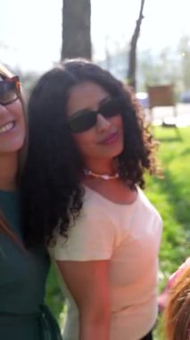 Çok ırklı bayan arkadaşlar güneşli bir park gününde neşeli anlar paylaşıyorlar, gizli selfie 'ler çekiyorlar ve birlikte vakit geçirirken arkadaşlığın tadını çıkarıyorlar.
