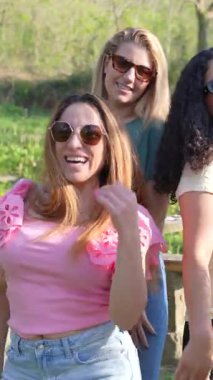 Güneşli park gününde dans eden ve neşeli anları kaydeden bayan arkadaşlar, akıllı telefonlar ve canlı moda ile kendiliğinden gelen enerjiyi paylaşıyorlar.