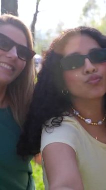 Çok ırklı kadın arkadaşlar kaynaşıyor, neşeli selfie çekerken güneşli park atmosferinin tadını çıkarıyorlar.