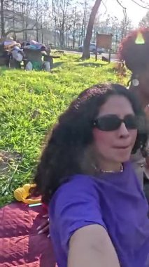 Piknik için toplanan kız arkadaşlar, selfie çekiyorlar ve neşe saçıyorlar yemyeşil bir parkta güneşli bir günün tadını çıkarıyorlar.