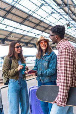 Pasaportlarını kontrol eden ve bir istasyonda trenlerini beklerken gülümseyen mutlu turist grubu.