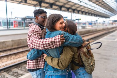 Tren istasyonunda birbirlerine sarılan üç mutlu öğrenci yolculukları için heyecanlı ya da tekrar buluştukları için mutlular.