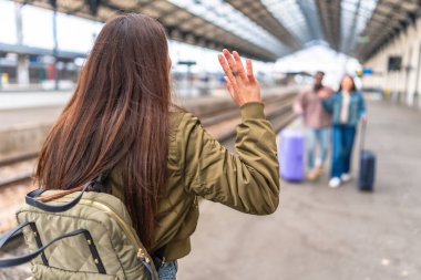 Bir tren istasyonuna gelen arkadaşlarına el sallayan genç bir kadın, seyahat ve arkadaşlık konsepti.